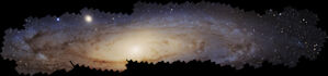 The Andromeda galaxy, a spiral galaxy, spreads across the image. It is tilted nearly edge-on to our line of sight so that it appears very oval. The borders of the galaxy are jagged because the image is a mosaic of smaller, square images against a black background. The outer edges of the galaxy are blue, while the inner two-thirds is yellowish with a bright, central core. Dark, dusty filamentary clouds wrap around the outer half of the galaxy’s disk. At 10 o’clock, a smaller dwarf elliptical galaxy forms a fuzzy, yellow blob. Hubble’s sharp vision distinguishes about 200 million stars within the image.