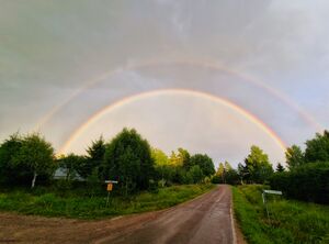 Photograph depicts a double rainbow over a country road.