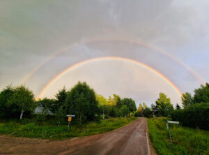 Photograph depicts a double rainbow over a country road.