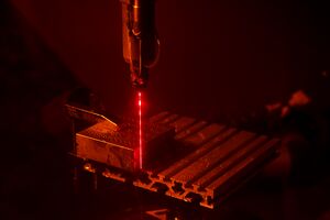 A red laser beam cutting through a metal block.